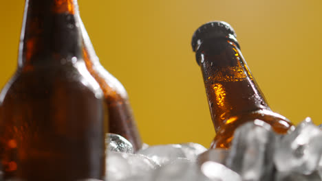 Nahaufnahme-Einer-Person,-Die-Eine-Glasflasche-Mit-Kaltem-Bier-Oder-Alkoholfreien-Getränken-In-Einen-Mit-Eis-Gefüllten-Eimer-Legt,-Um-Sie-Vor-Gelbem-Hintergrund-Abzukühlen